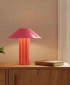 Table lamp with a pink and orange striped base on a wooden surface.