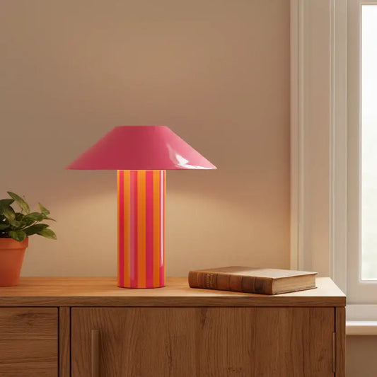 Table lamp with a pink and orange striped base on a wooden surface.