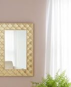 Decorative mirror with geometric pattern on a wall with a potted plant below.
