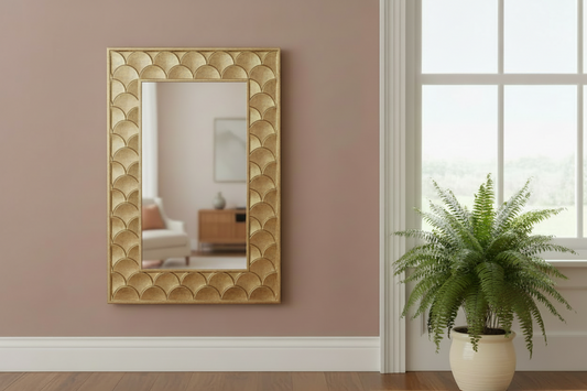 Gold decorative mirror on a wall with a plant in the foreground