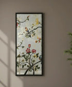 Framed floral artwork with birds on a wall next to a plant