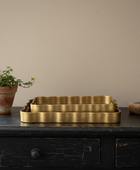 Brass tray on a dark wooden surface with a plant and book against a beige wall.
