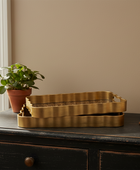Gold tray on a dark wooden surface with a plant and book in the background.