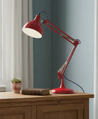 Red adjustable desk lamp on a wooden surface with a window and plant in the background