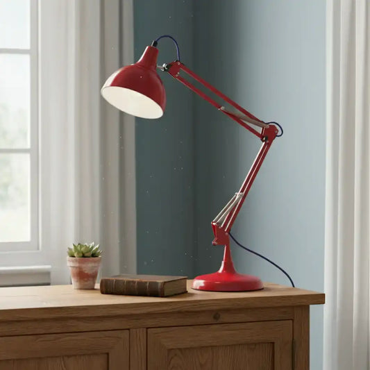 Red adjustable desk lamp on a wooden surface with a window and plant in the background