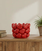 Red heart-shaped candle holder on a wooden surface with a plant and books in the background.