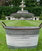 Metal basin on grass with a fountain and garden in the background