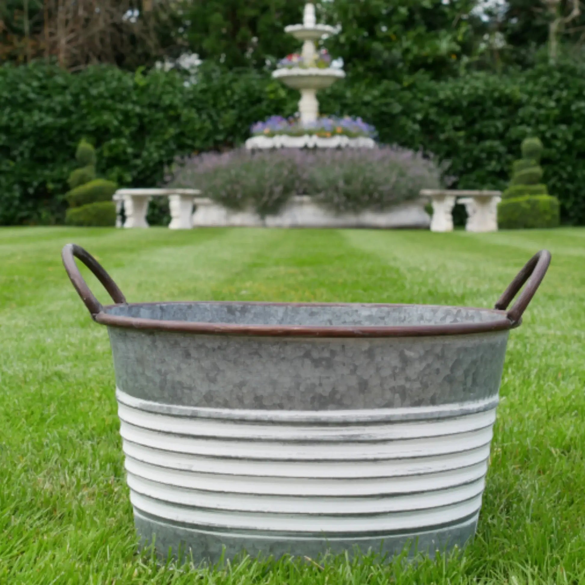 Metal basin on grass with a fountain and garden in the background