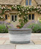 Decorative metal tub in a garden with a house and flowers in the background