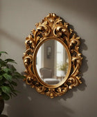 Decorative gold mirror with intricate designs on a wall next to a plant.