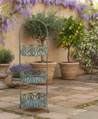 Decorative metal plant stand in a garden setting with potted plants and flowers.