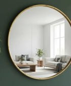 Round mirror with gold frame on a green wall reflecting a living room.
