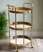 Gold three-tiered serving cart with marble-like surface on a wooden floor.