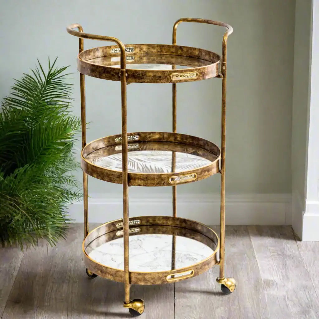 Gold three-tiered serving cart with marble-like surface on a wooden floor.