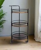 Black and bronze three-tier rolling cart in a room with plants and curtains.