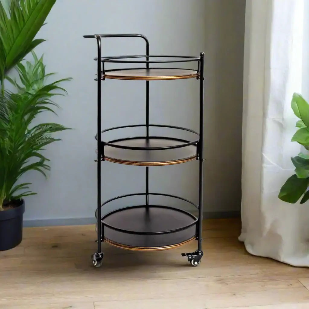 Black and bronze three-tier rolling cart in a room with plants and curtains.