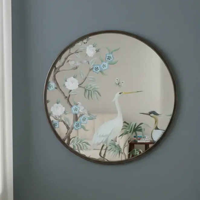 Round wall mirror with floral and bird design on a gray wall