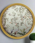 Decorative wall mirror with floral and bird design in a gold frame on a gray wall.
