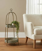 Decorative metal plant stand with a plant next to a beige armchair in a room with a window.
