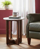 Small round wooden side table with a white marble top next to a green leather sofa in a living room.