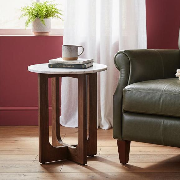 Small round wooden side table with a white marble top next to a green leather sofa in a living room.