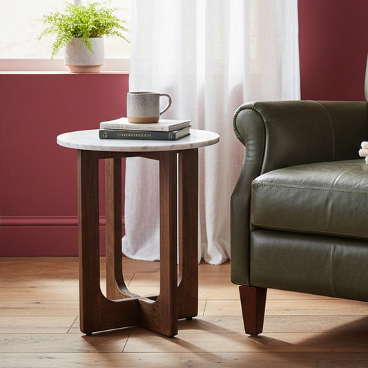 Small round wooden side table with a white marble top next to a green leather sofa in a living room.