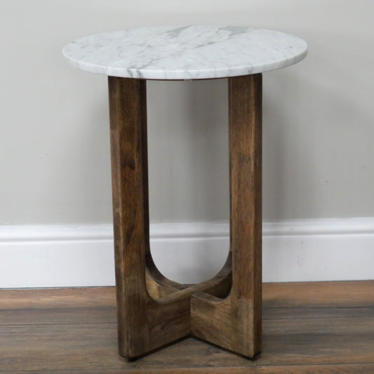 Small round table with marble top and wooden base against a plain wall.