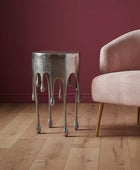 Metallic side table with unique design next to a pink armchair against a red wall.