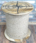 Wooden stool made from a rope spool with a compass design on top, against a brick wall.