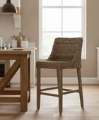 Brown wicker bar stool in a kitchen setting with wooden table and white cabinets.