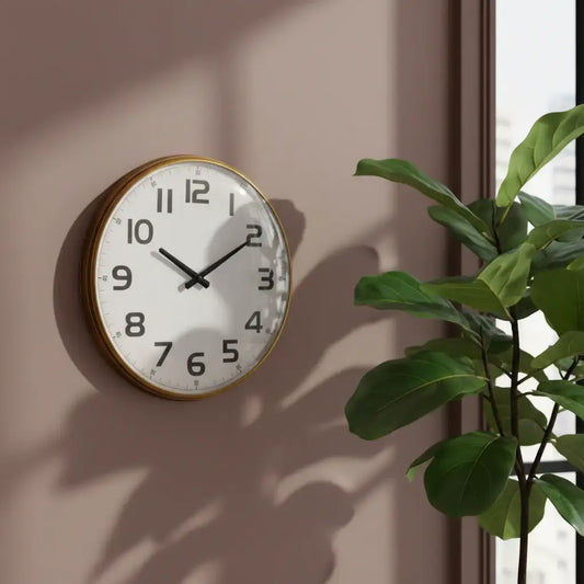 Round wall clock with gold frame on a beige wall next to a green plant