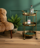 Gold bar cart with bottles in a room with a green wall and fur chair.