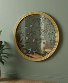 Round gold-framed mirror with floral design on a green wall