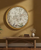 Decorative wall art with floral and bird design in a gold frame on a mustard yellow wall.