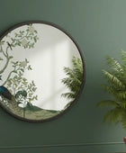 Decorative mirror with peacock design on a green wall next to a potted plant.