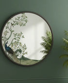 Round decorative mirror with peacock design on a green wall