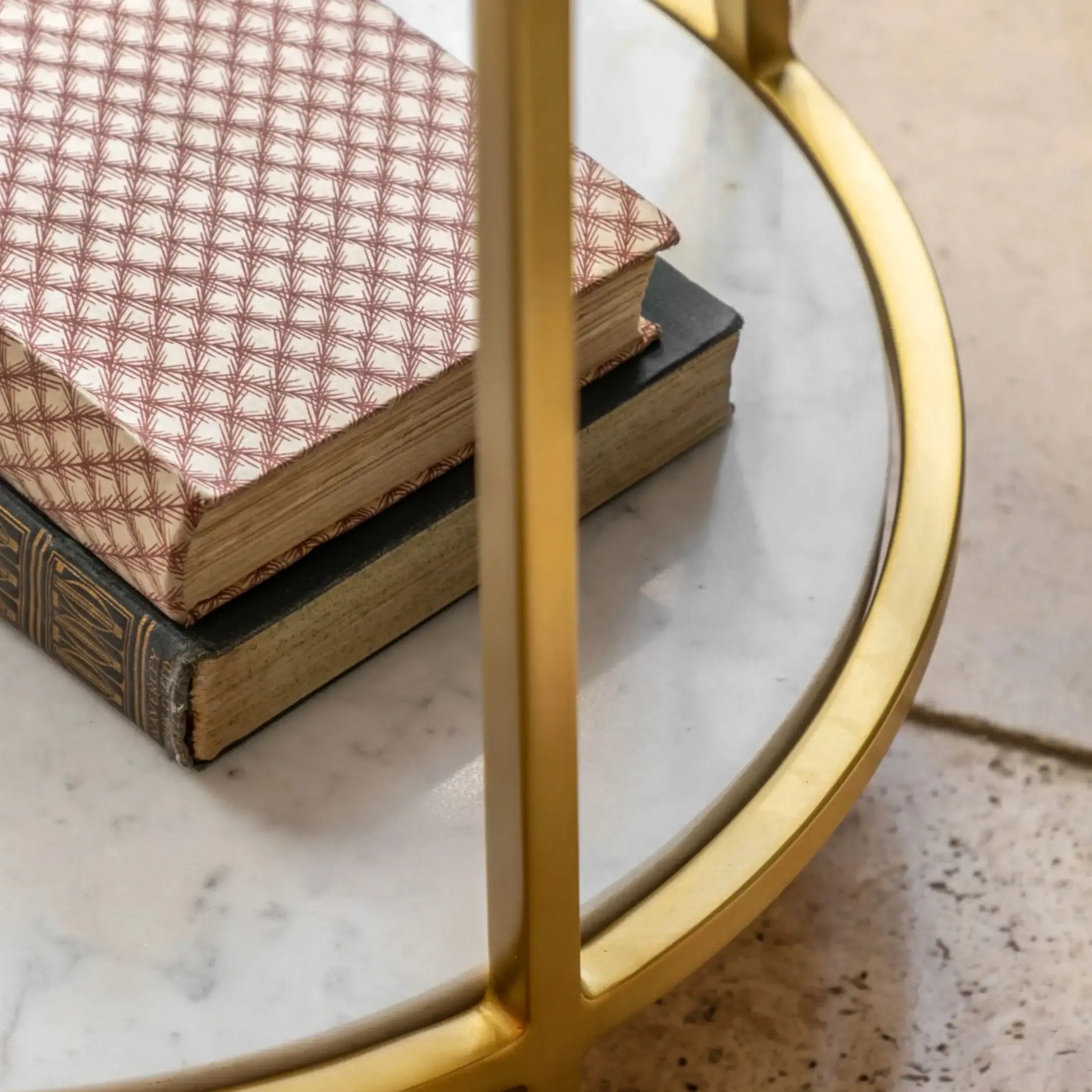 Two books stacked on a round marble table with a gold frame.