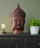 Decorative Buddha head on a wooden cabinet with a light bulb and plant