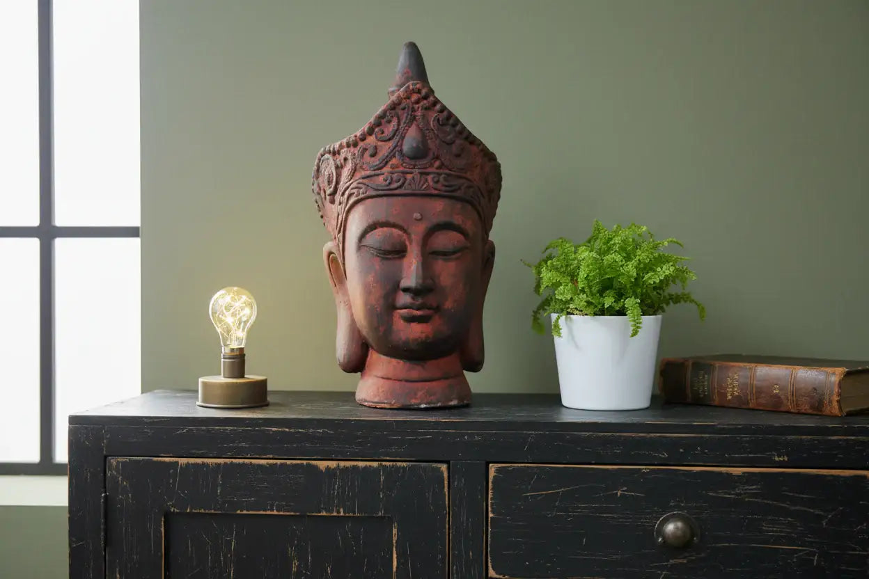 Decorative Buddha head on a wooden cabinet with a light bulb and plant