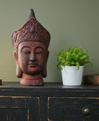 Decorative Buddha head, potted plant, and light bulb on a dark wooden surface with a green wall background.