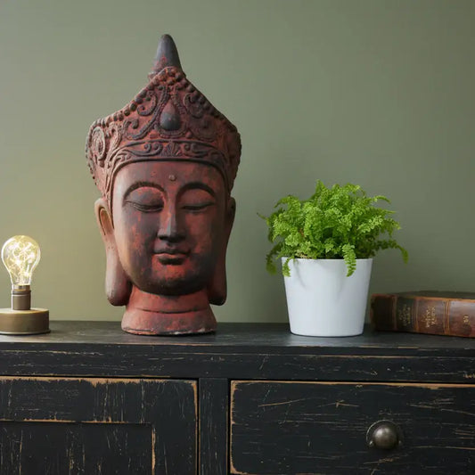 Decorative Buddha head, potted plant, and light bulb on a dark wooden surface with a green wall background.