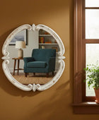Decorative wall mirror on a brown wall with a blue armchair and window in the reflection.