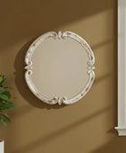 Decorative oval mirror on a beige wall with a plant and window in the background