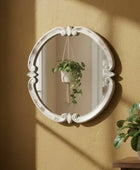 Decorative oval mirror with intricate details on a beige wall.