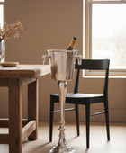 Silver ice bucket with a bottle of champagne on a wooden table in a room with a window.