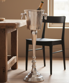 Silver champagne bucket with a bottle on a wooden table in a room with a window.