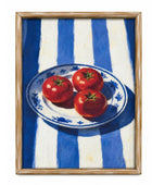 A framed still life painting featuring three red tomatoes on a blue and white patterned plate, set against a blue and white striped background, enclosed in a light wood frame.