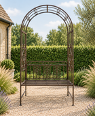 A dark brown wrought iron garden bench with an arched trellis design, set in a landscaped garden on a gravel path with a stone house and green hedges in the background.