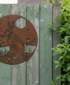 Decorative metal hare sculpture on a wooden fence with greenery in the background