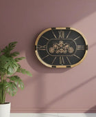 Decorative wall clock with gold frame and black face on a pink wall, next to a potted plant.